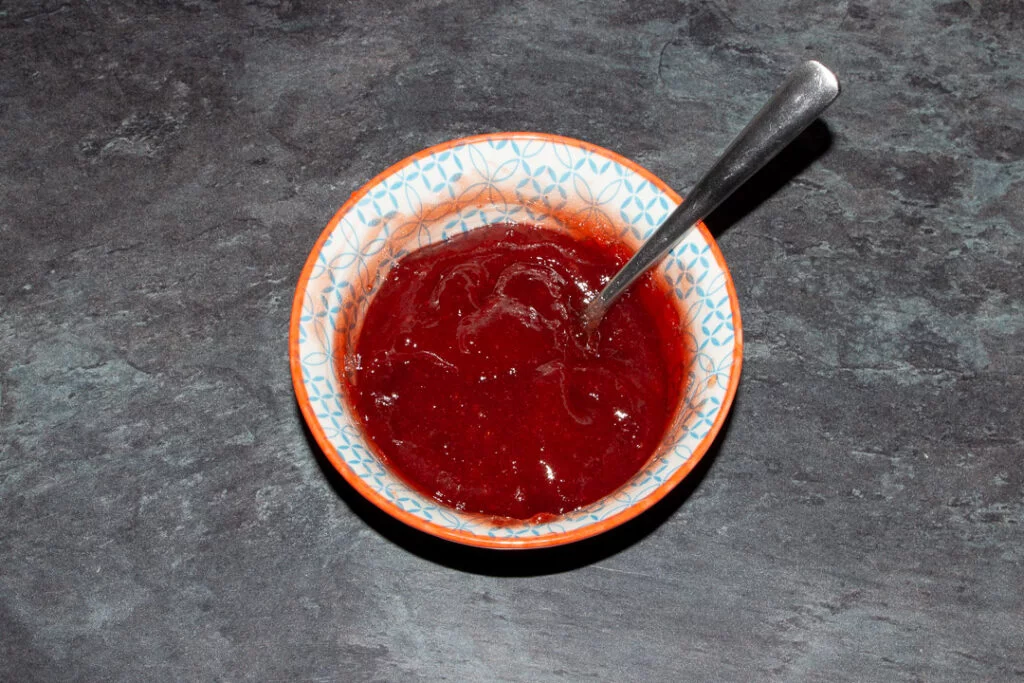A small bowl of jam that's been mixed to smooth it with a metal teaspoon