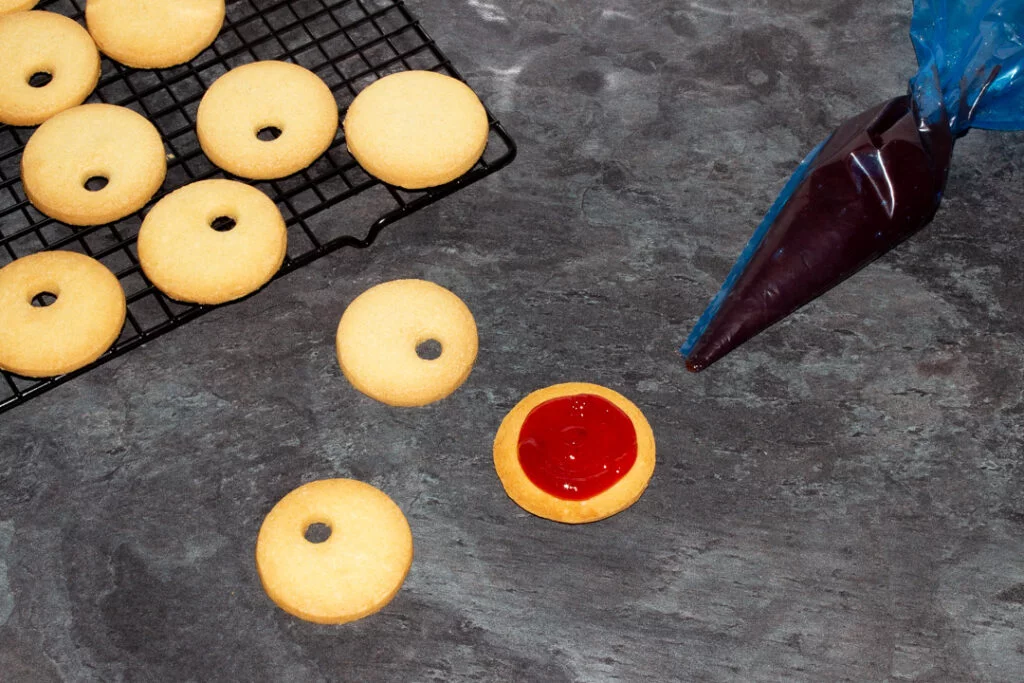 Jam being piped onto cookies using a blue disposable piping bag