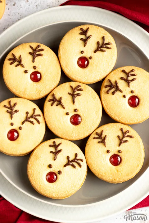 A plate of Reindeer cookies set on a second plate and a red linen napkin. Set on an off white backdrop in the background.