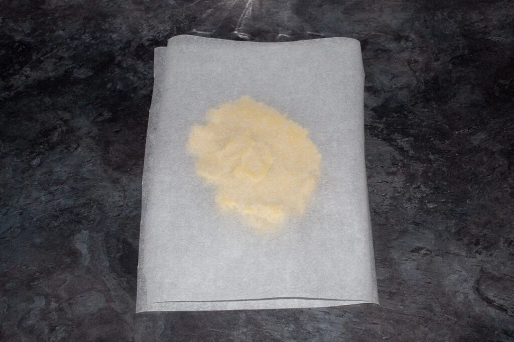 Cookie dough pressed between two sheets of baking paper ready for rolling