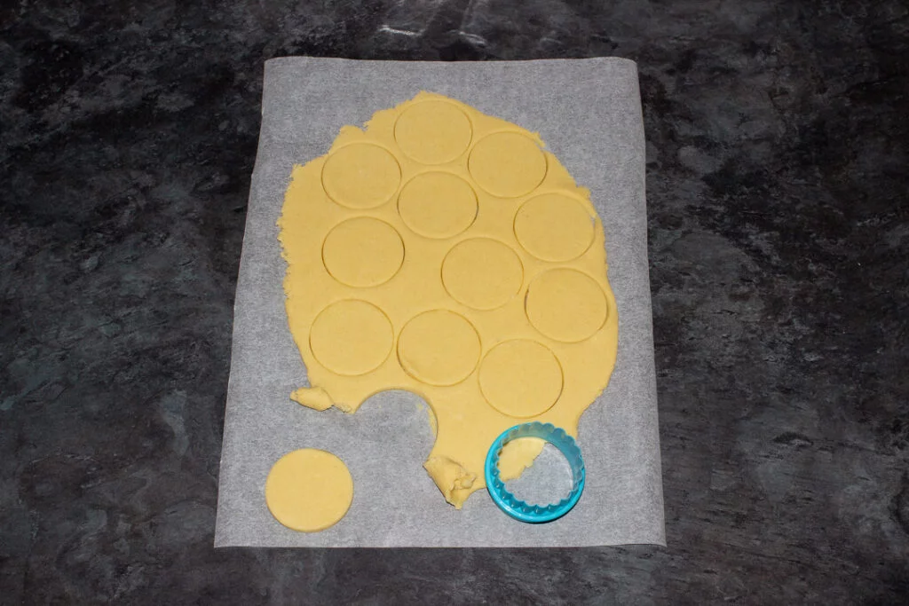 Cookie dough rolled out and cut on a sheet of baking paper with a small circular cookie cutter