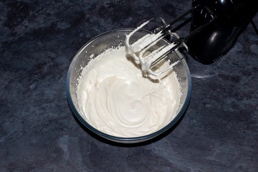 Whipped Baileys and double cream in a glass bowl with an electric hand whisk