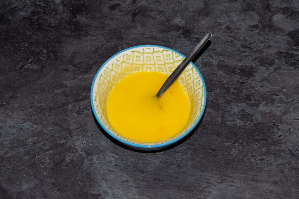 Melted butter in a small blue bowl with a metal spoon