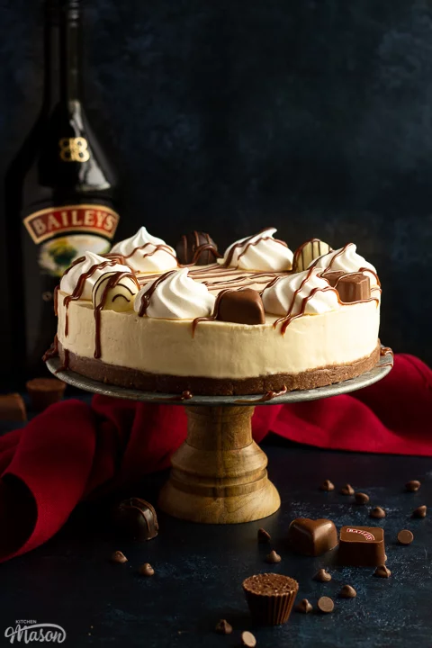 A whole Baileys cheesecake on a cake stand with a red linen napkin underneath
