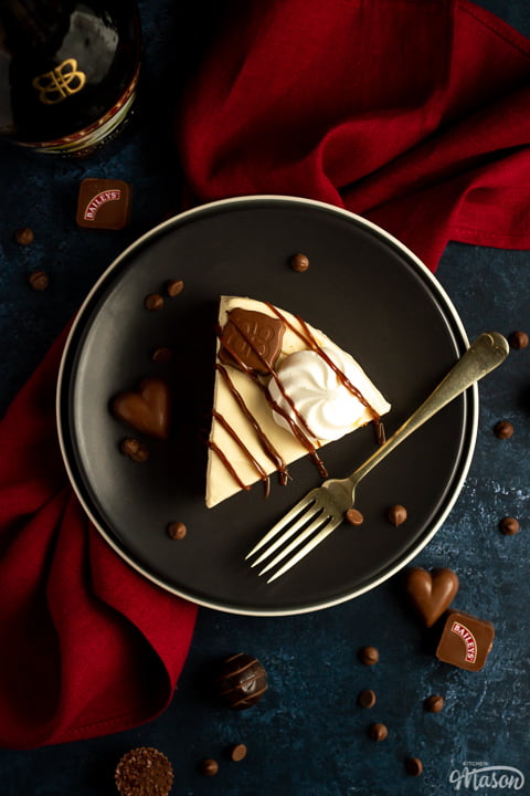 A slice of no bake Baileys cheesecake on a plate with a fork over a red napkin