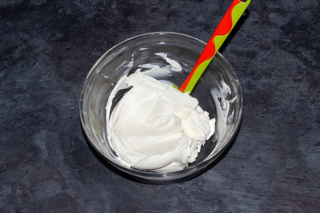 Cream cheese that's been beaten slightly to soften it in a glass bowl with a green spatula