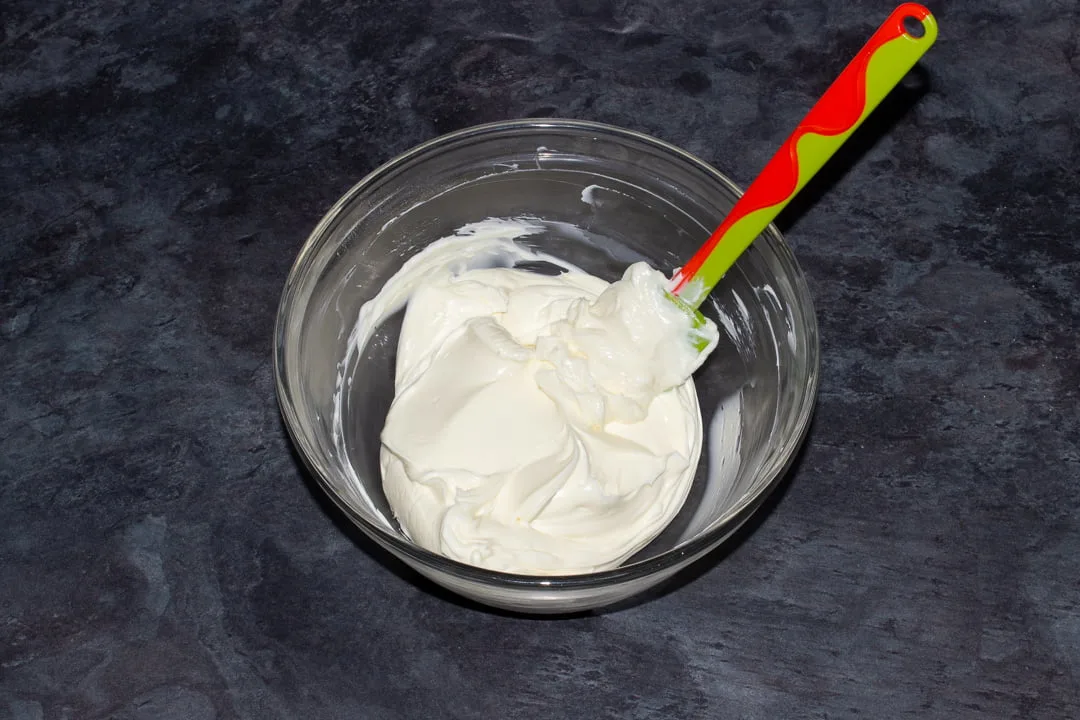 Cream cheese and icing sugar that's been mixed together in a glass bowl with a green spatula