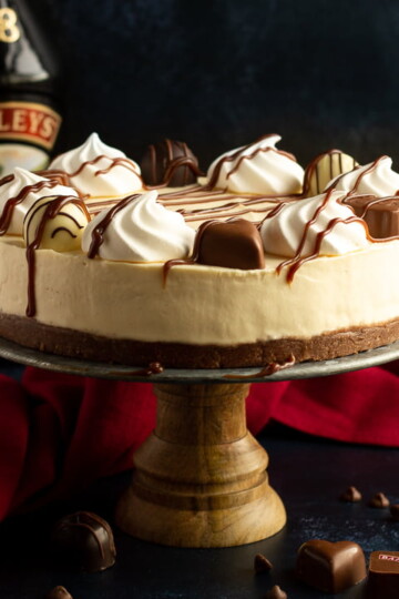 A no bake Baileys cheesecake on a cake stand set over a deep blue background with a red linen napkin.