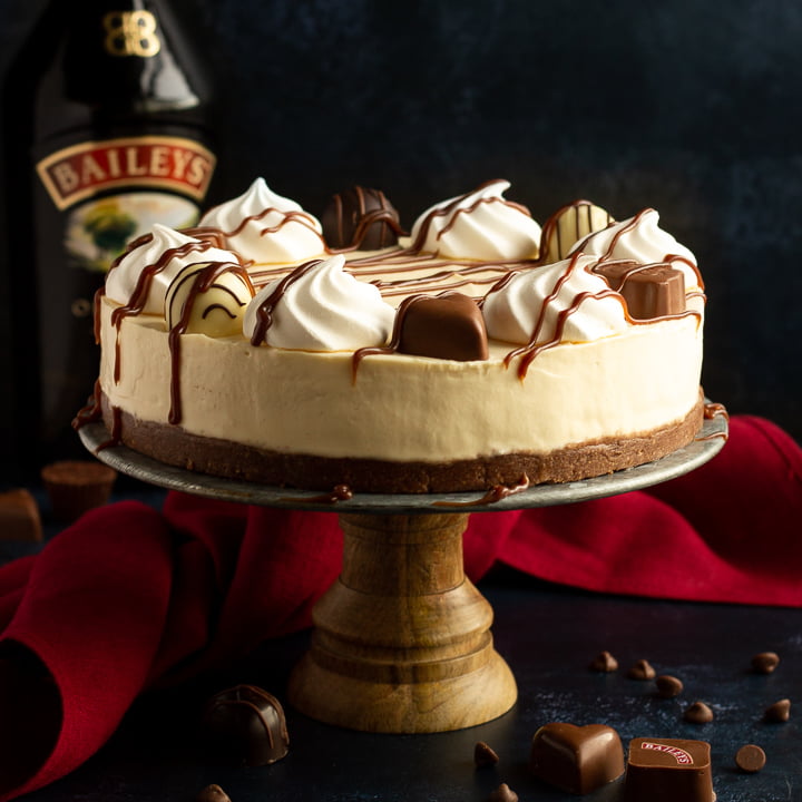 A no bake Baileys cheesecake on a cake stand set over a deep blue background with a red linen napkin.