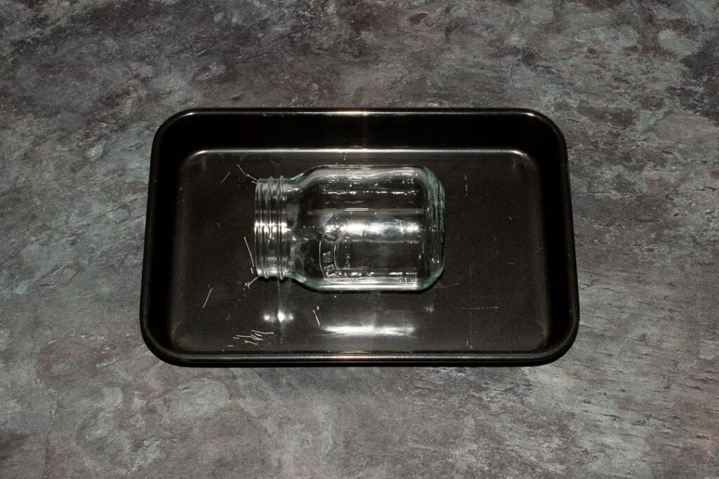 a glass jar on a black baking tray ready for sterilising in the oven