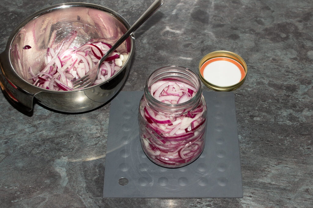 Hot sliced red onions being stuffed into a hot sterilised glass jar