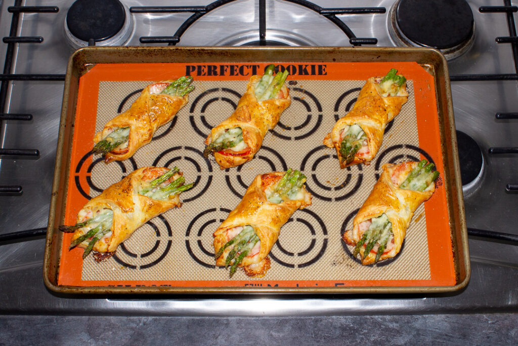 6 baked asparagus puff pastry parcels on a lined baking tray