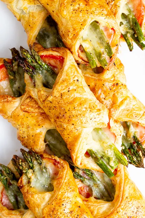 A close up of some asparagus puff pastry parcels on a white serving plate