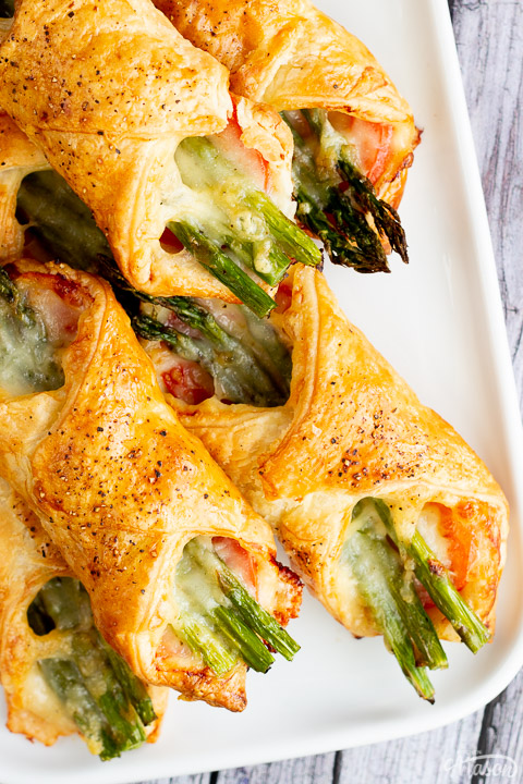 A close up of some asparagus puff pastry parcels on a white serving plate