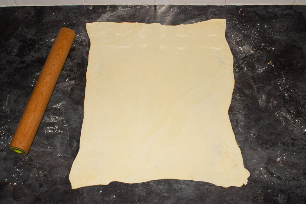 A sheet of puff pastry rolled out with a rolling pin on a lightly floured work surface