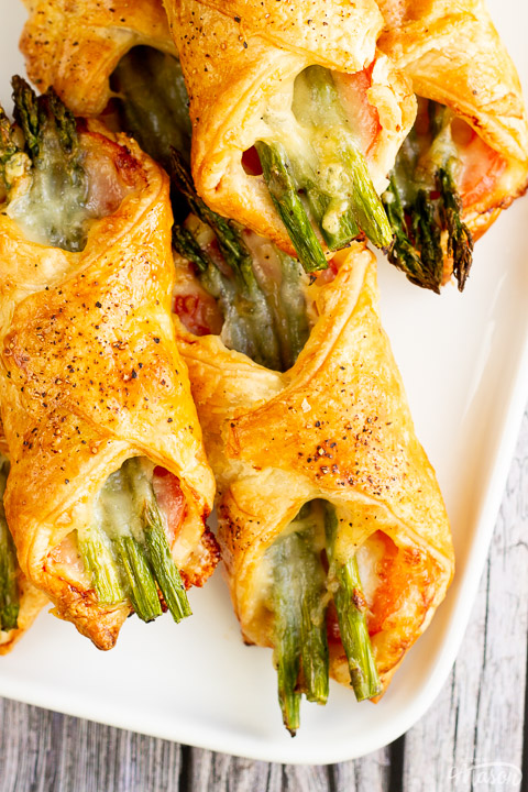 A close up of some asparagus puff pastry parcels on a white serving plate