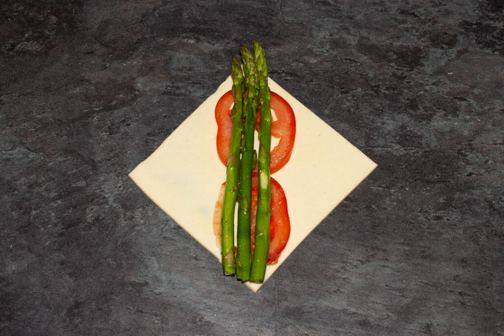 A square of puff pastry on the diagonal with two thin slices of tomato on top and 3 trimmed asparagus tips