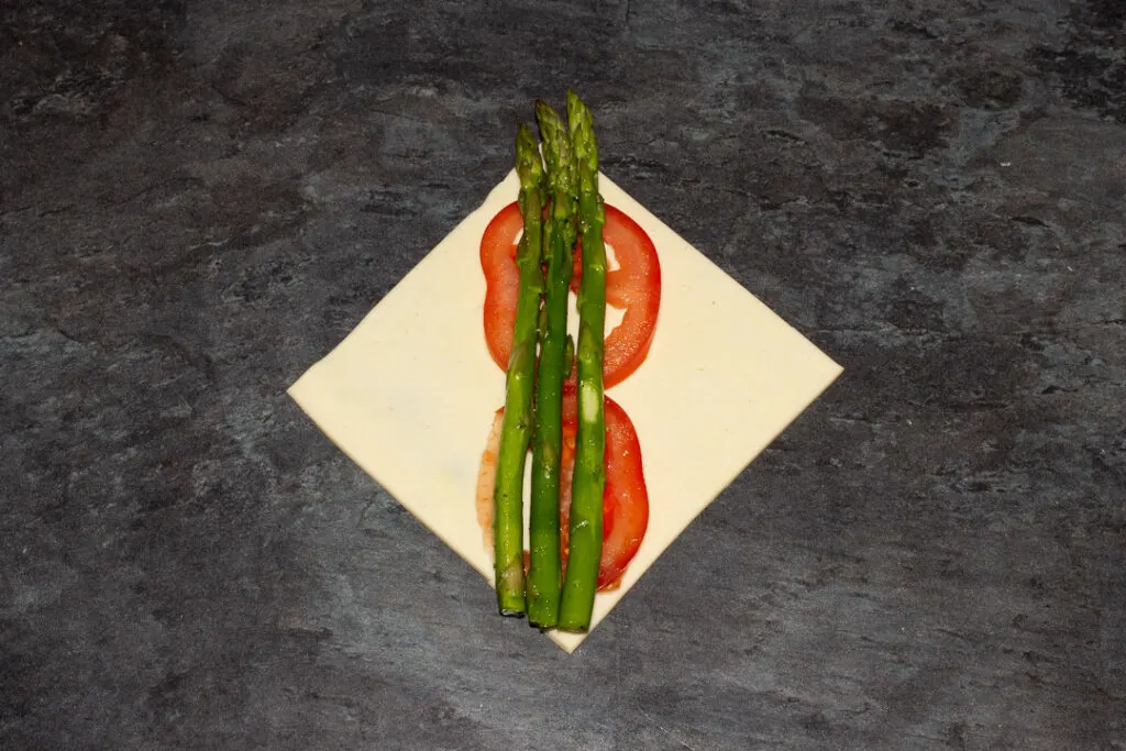 A square of puff pastry on the diagonal with two thin slices of tomato on top and 3 trimmed asparagus tips