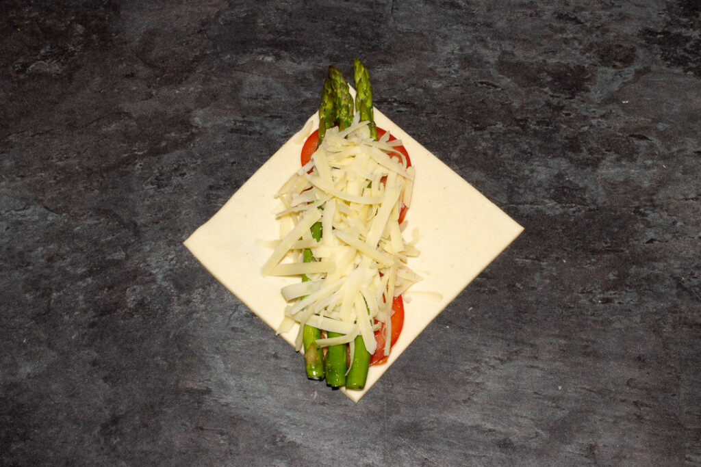 A square of puff pastry on the diagonal with two thin slices of tomato on top, 3 trimmed asparagus tips and a little grated gruyere cheese