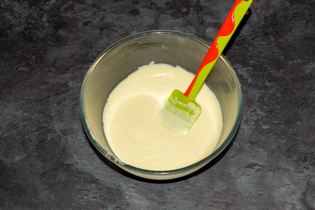 Melted butter and white chocolate in a glass bowl on a kitchen worktop with a green spatula