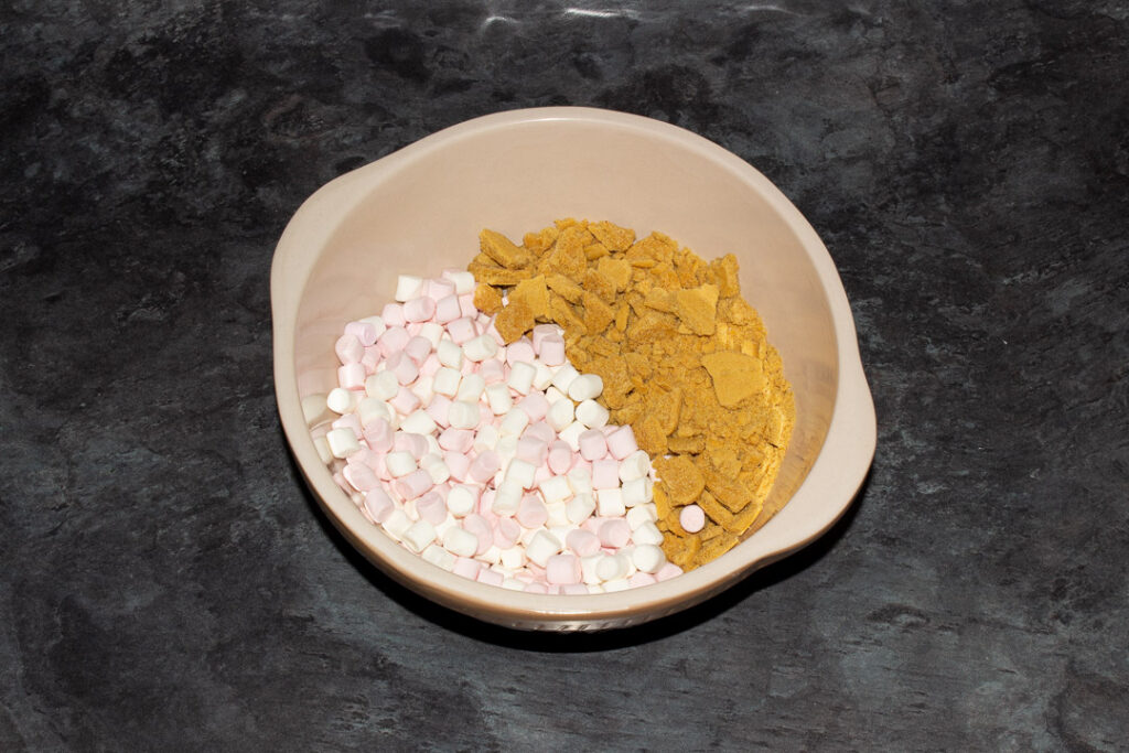 Pink and white mini marshmallows and crushed gingerbread biscuits in a large bowl on a kitchen worktop
