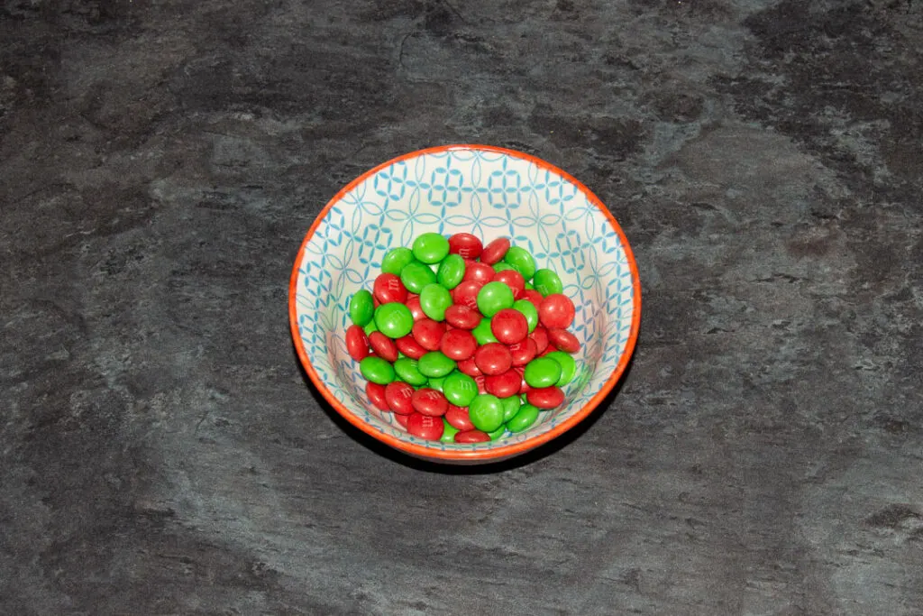 Green and red M&M's in a small bowl on a kitchen worktop