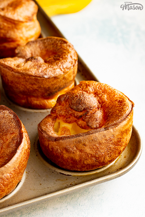 Yorkshire puddings in a Yorkshire pudding pan with a mustard yellow napkin in the background.