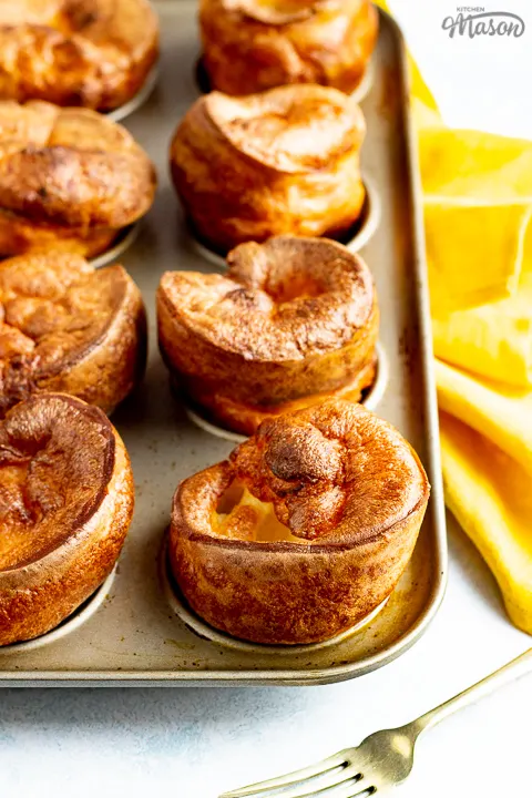 Yorkshire puddings in a Yorkshire pudding pan with a mustard yellow napkin and a fork in the background.