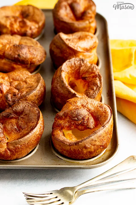 Yorkshire puddings in a Yorkshire pudding pan with a mustard yellow napkin and 3 forks in the background.