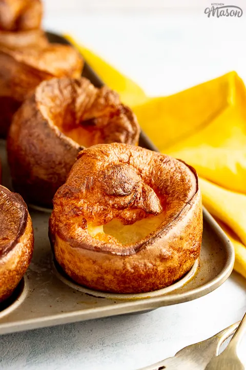 Yorkshire puddings in a Yorkshire pudding pan with a mustard yellow napkin and 2 forks in the background.