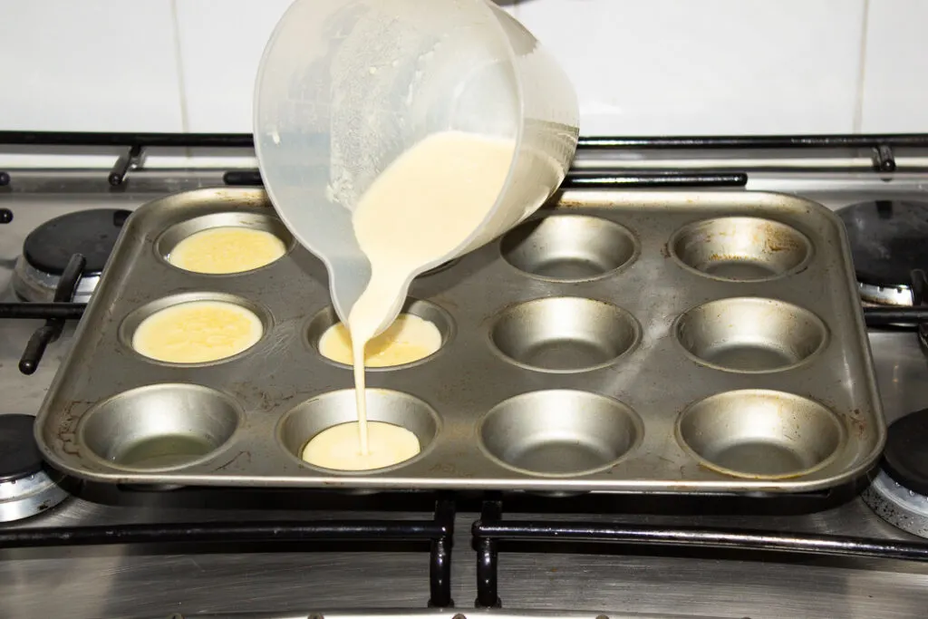 Yorkshire pudding batter being poured into a yorkshire pudding tin filled with hot oil