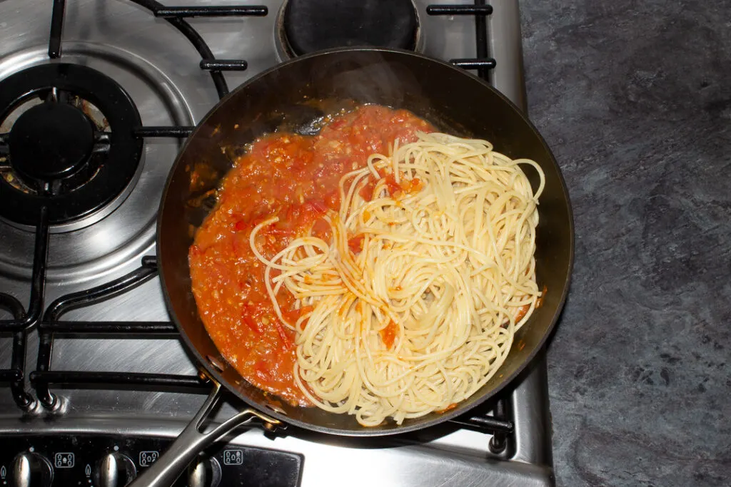 Tomato spaghetti sauce in a frying pan on the stove with freshly cooked spaghetti.