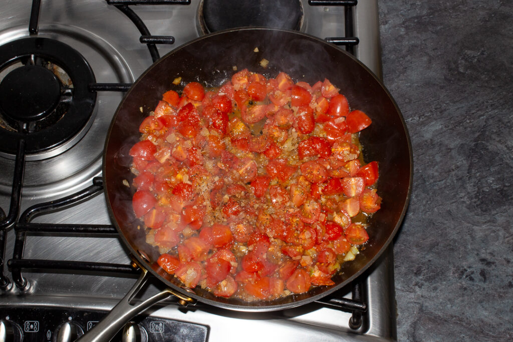 Onion, garlic, chopped cherry tomatoes, balsamic vinegar and salt and pepper in a frying pan cooking on the stove