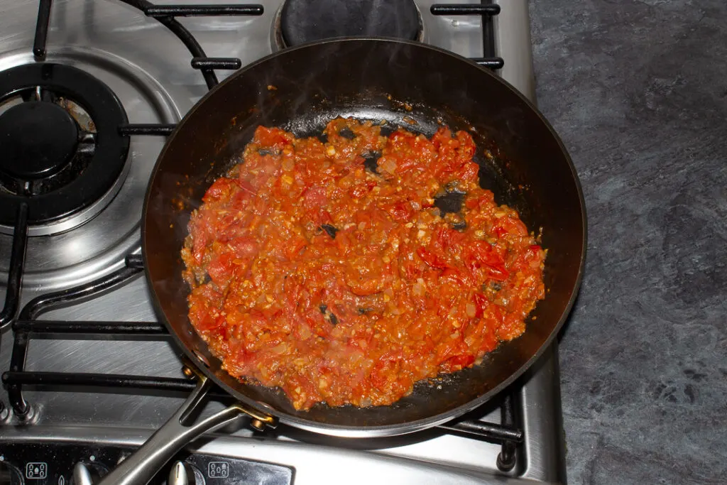 Cooked and reduced onion, garlic, cherry tomatoes, balsamic vinegar and salt and pepper in a frying pan on the stove