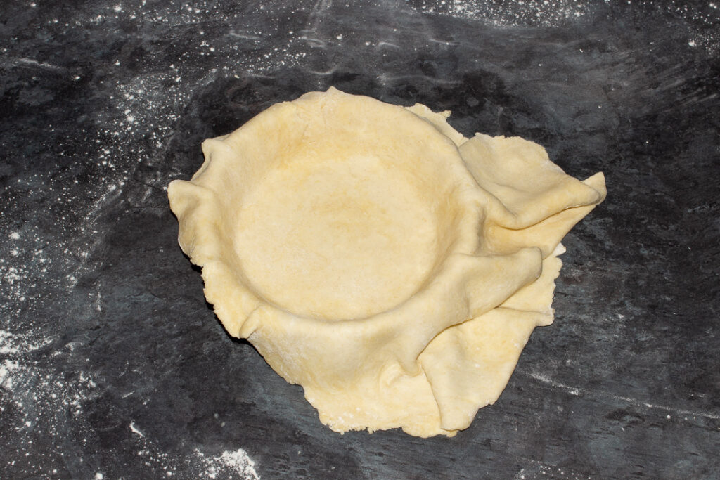 Shortcrust pastry draped over a pie dish on a floured worktop