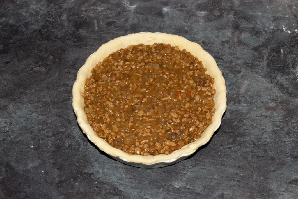 A pie dish lined with shortcrust pastry filled with vegetarian soya mince and onion