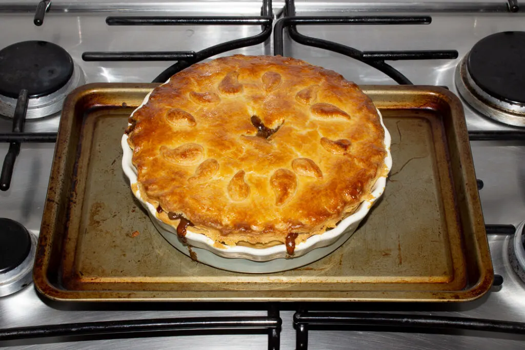 A baked vegetarian mince and onion pie on a baking tray on the stove top