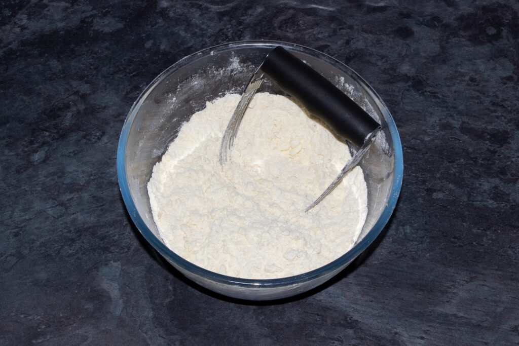 Flour, salt and butter that's been rubbed together to form crumbs, in a glass mixing bowl.