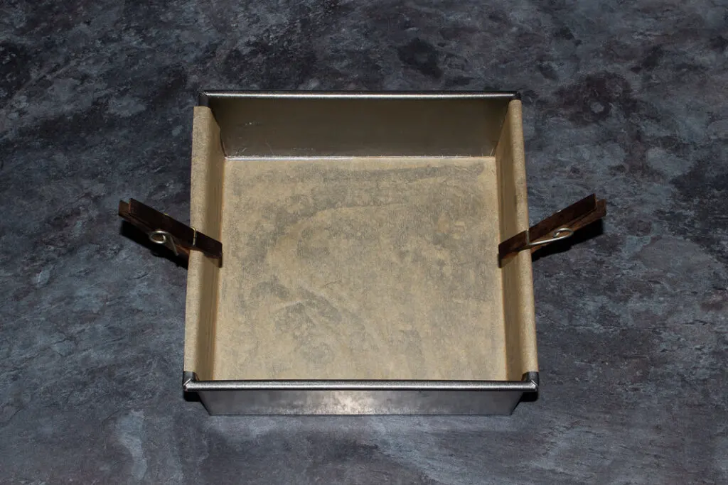 A square baking tin lined with baking paper and held on by two pegs