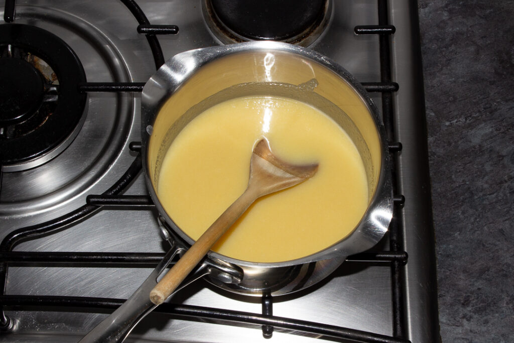 Melted caramel ingredients in a saucepan on the hob with a wooden spoon.