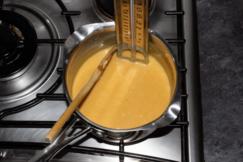 Caramel that has been cooked to 107ºC in a saucepan on the hob with a wooden spoon and a thermometer inside.