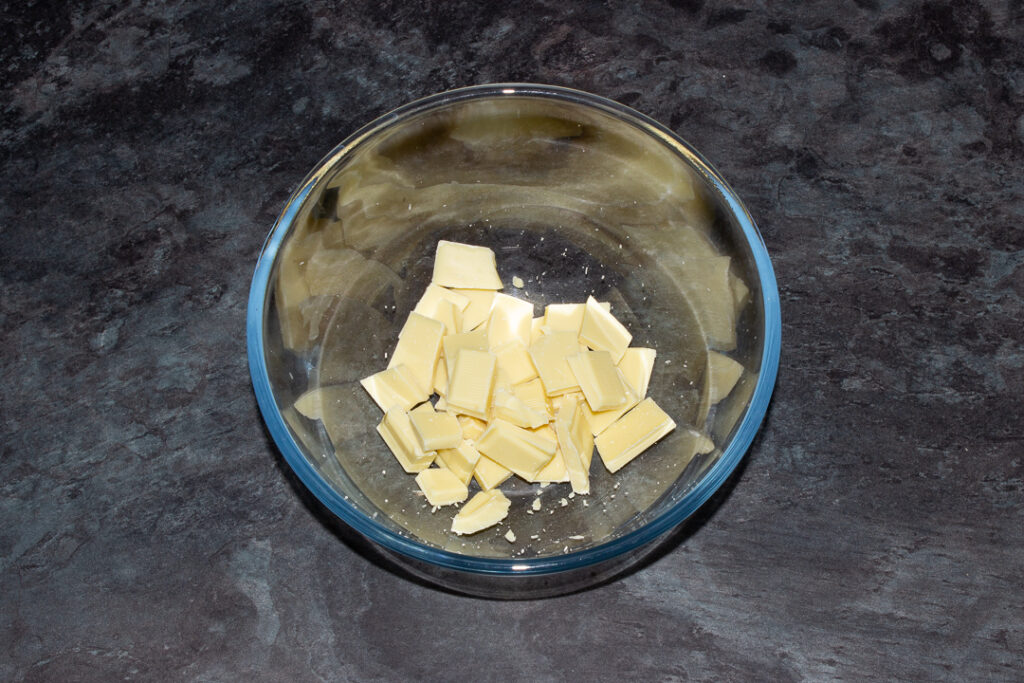 Broken white chocolate in a glass bowl on a kitchen worktop.