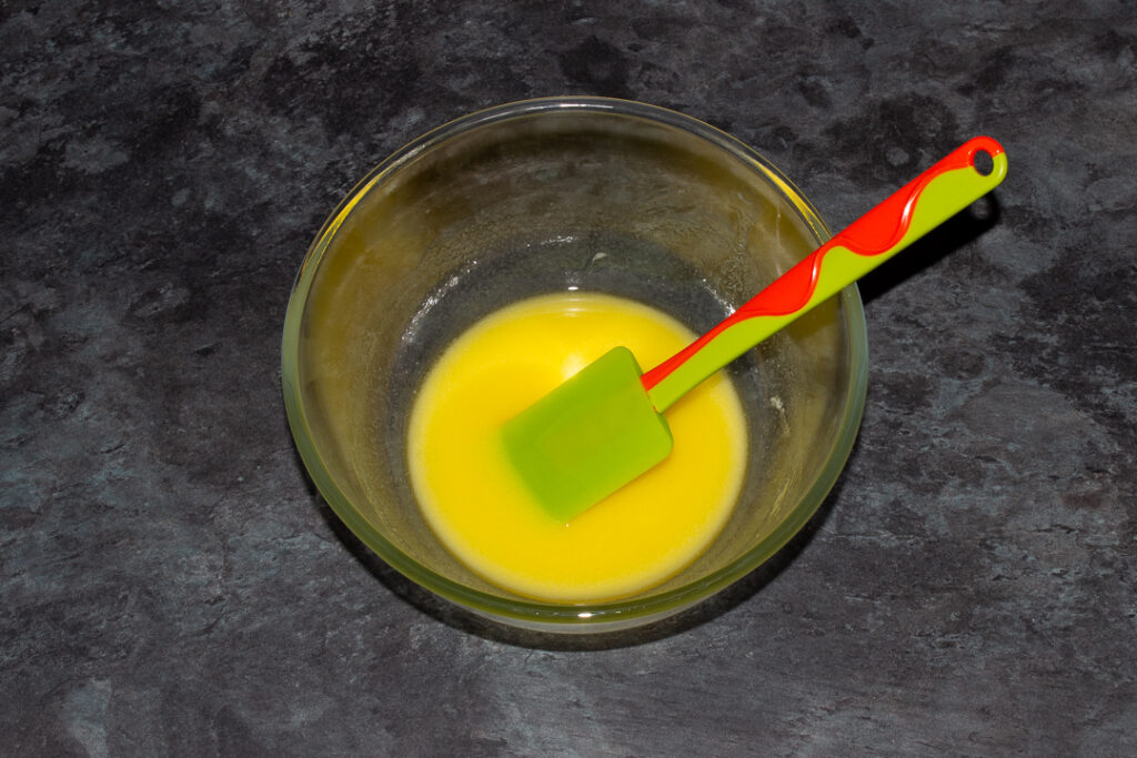 Melted butter in a glass mixing bowl with a green spatula