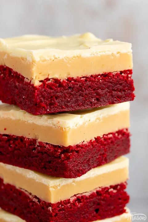 A close up of 4 red velvet millionaire brownies in a stack set against a mottled light background.