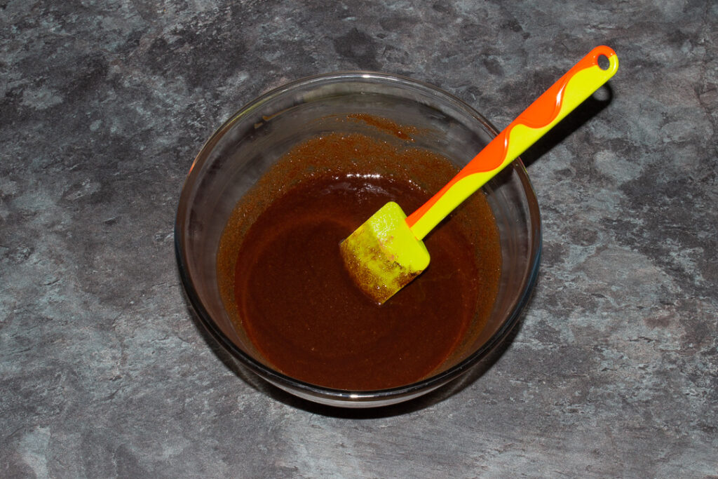 Melted butter, sugar and cocoa butter mixed together in a glass bowl with a green spatula