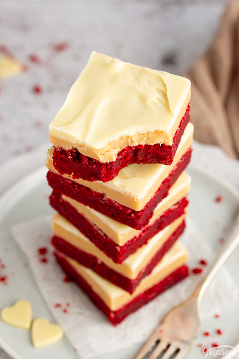 A stack of 5 red velvet millionaire brownies set on two stacked plates with a fork on the side. The top one has a bite taken out of it.