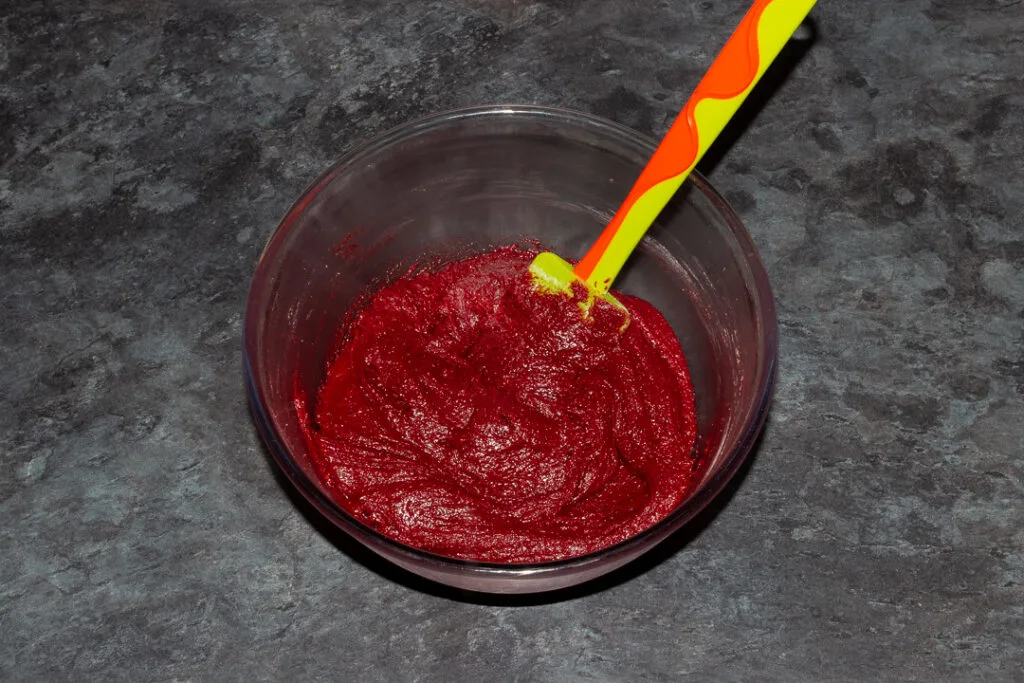 Red velvet brownie batter in a glass bowl with a green spatula.
