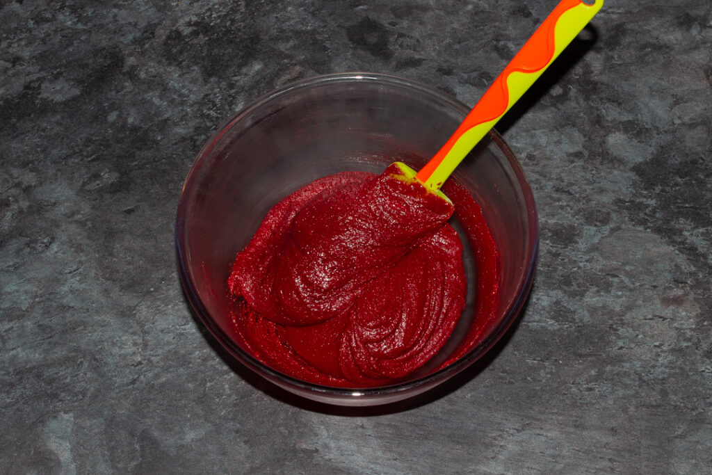 Red velvet brownie batter and vinegar in a glass bowl with a green spatula.