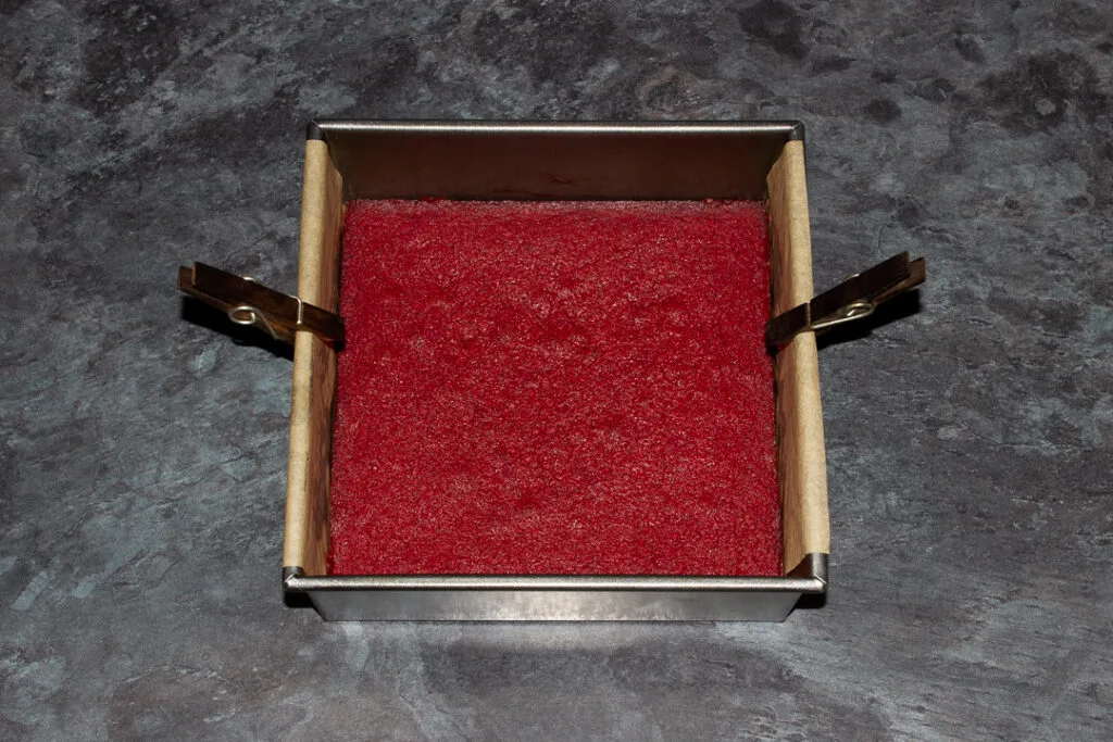 Baked red velvet brownie in a lined square baking tin with a peg on each side.