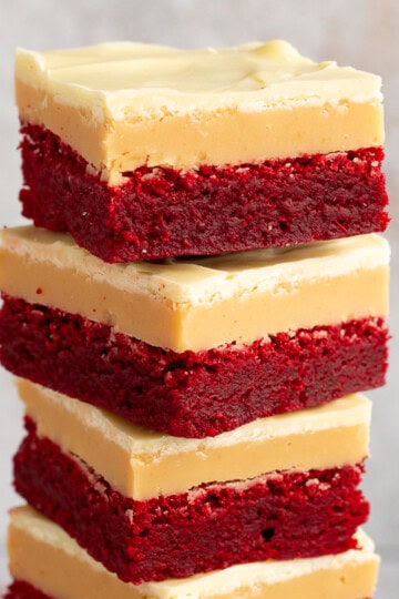A close up of 4 red velvet millionaire brownies in a stack set against a mottled light background.